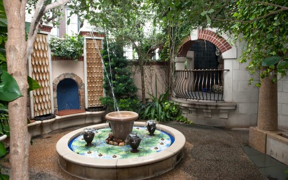 a small fountain in the middle with building structures and green trees surrounding it