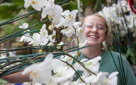 student smiling at camera surrounded by white orchid blooms