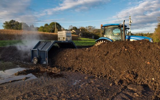 A tractor pulling a compost turner over a pile of dirt.
