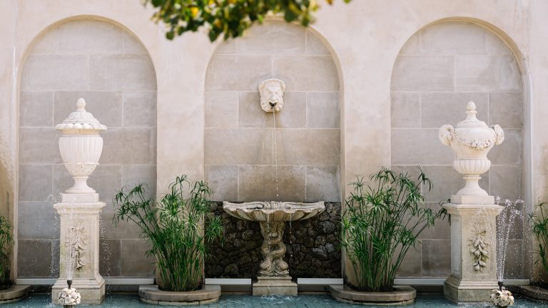 Three arches carved into a stone wall display fountain features and greenery.