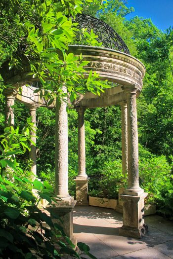 A stone decorative gazebo stands tall under green trees