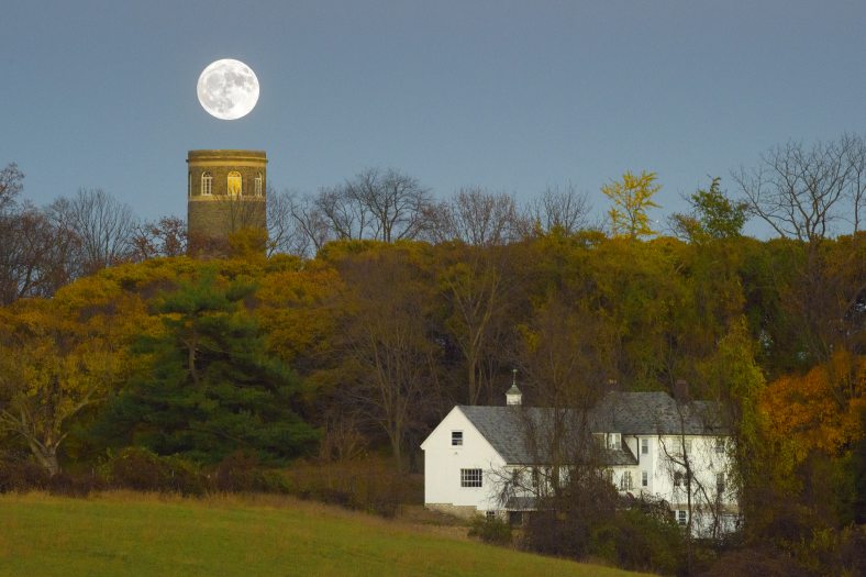 A white farmhouse set in a rolling landscape with a full moon in the sky.