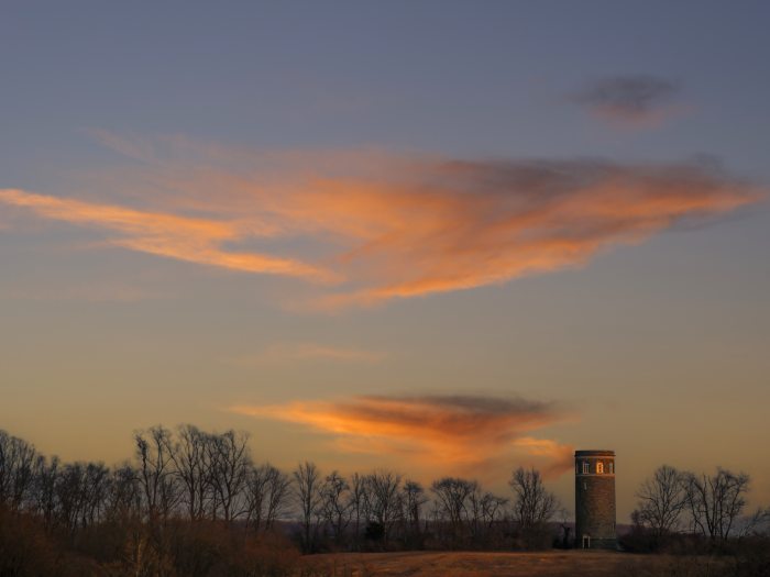 A sunset shot showing a line of trees and a stone tower in the distance.