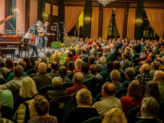A large audience watches a band of people playing instruments on stage