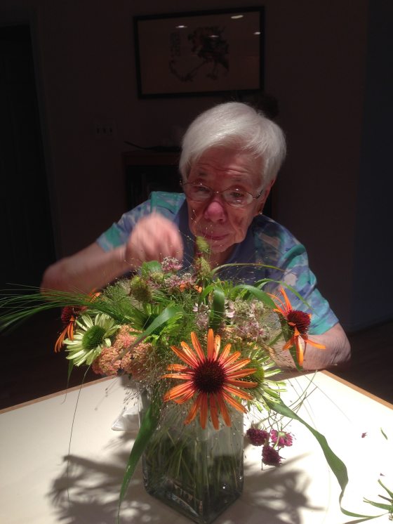 a person at a table arranging orange flowers and leaves in a vase