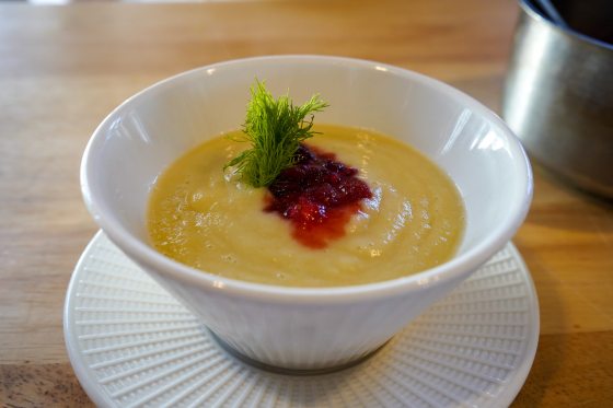 a bowl of yellow bisque topped with pureed cranberry and fennel