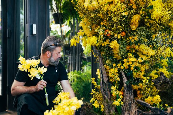 A person bending down next to a large floral display of yellow varieties of flowers..
