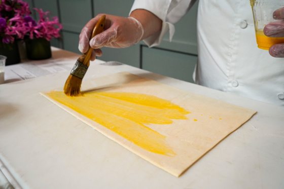 A person using a brush to apply an egg wash on pastry dough.