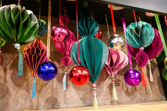 A variety of paper ornaments hanging in a range of colors amid glass ball ornaments.