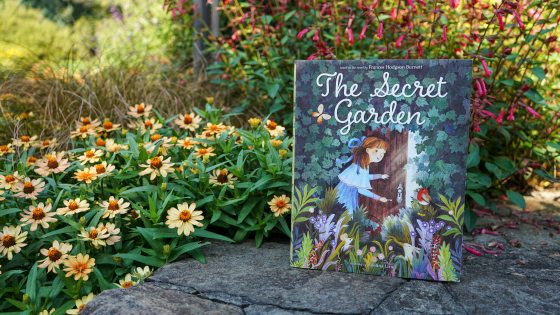 A book titled "The Secret Garden" poised on a stone ledge in front of blooming flowers.