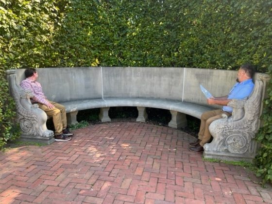 Two people sitting at opposite ends of a curved stone bench. 