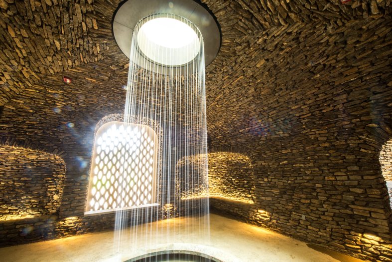 A circular water fall of small water streams drops from the ceiling in a stone grotto